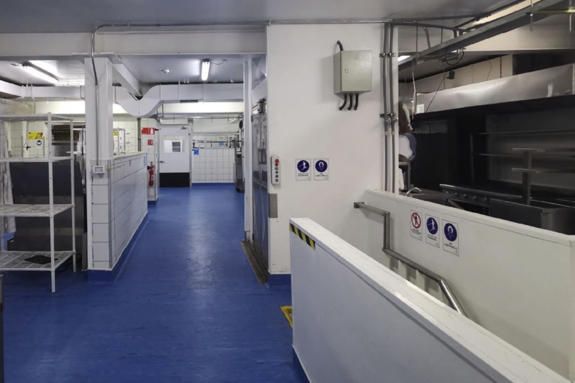 Cocina industrial remodelada, con piso epóxico azul, mesones de acero inoxidable y campanas