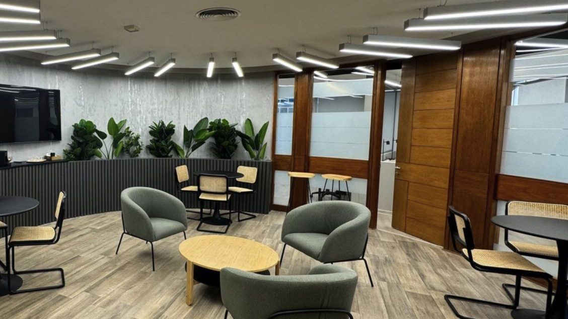 Sala de estar de las oficinas remodeladas de CIS Ingenieros, con sillones verdes, mesas de madera, jardineras y luminarias lineales